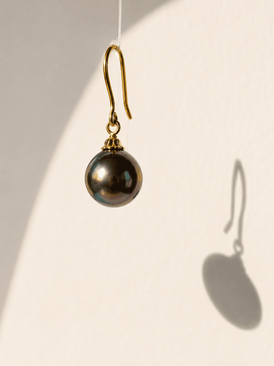 AI-generated editorial product shot of a Tahitian black pearl drop earring with a hard sunlight shadow, created by Raechal AI